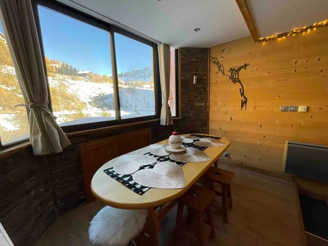 Le coin repas de l'Elisoun devant la baie vitrée, avec la montagne au soleil